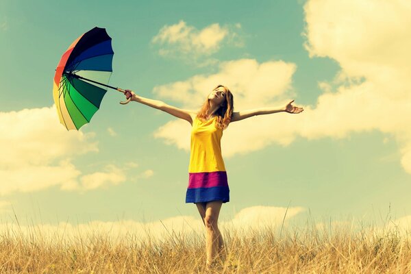 Chica en el campo con un paraguas multicolor