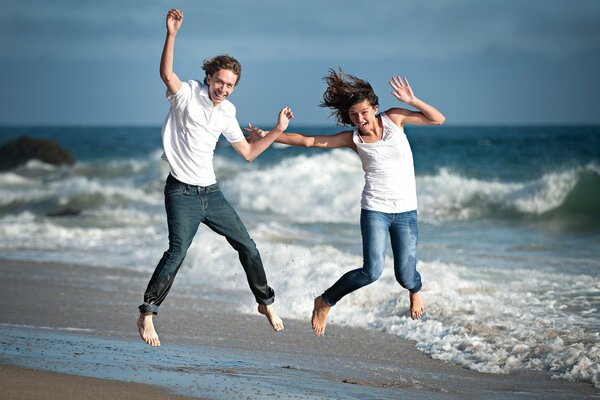 A girl with a guy on the sand near the sea jumping with happiness