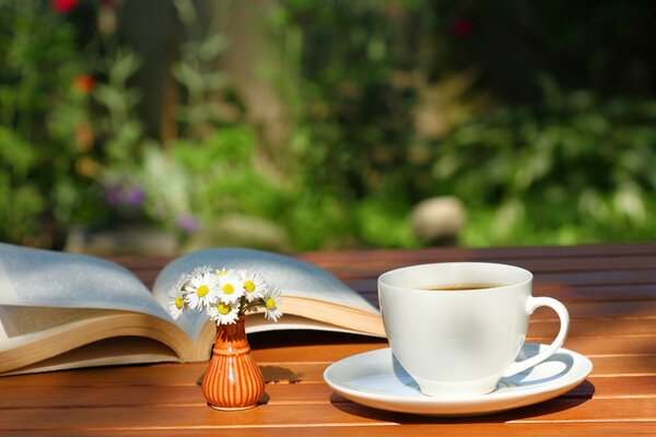 Natura morta di una tazza di tè, un bouquet di margherite in un piccolo generale e un libro