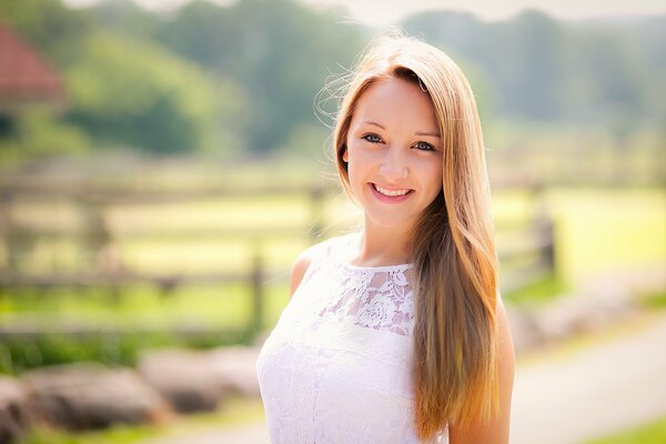 Cute girl in a white lace dress in summer on the background of a village fence