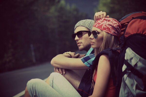 A young couple with hiking backpacks sitting on the road