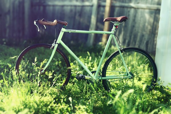 Bicicleta turquesa fija en la hierba contra el fondo de la cerca