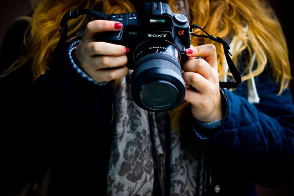 Chica con el pelo rojo y esmalte rojo en las uñas sostiene una cámara