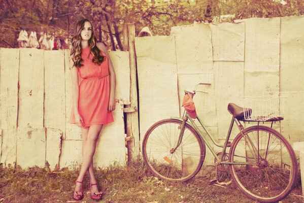 Ragazza carina con bicicletta su sfondo di recinzione