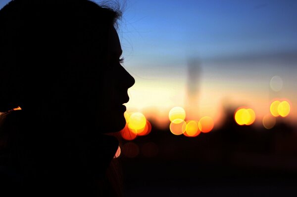 Profil de la jeune fille sur fond de coucher de soleil urbain