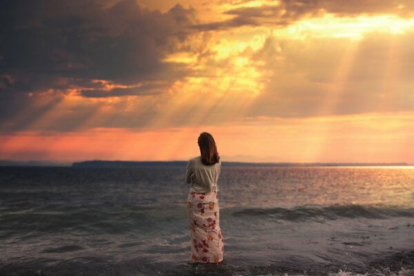 Fille en jupe longue regarde le coucher de soleil sur la mer