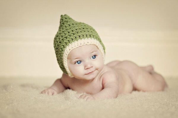 Младенец в вязанной зеленой шляпе лежит на животе