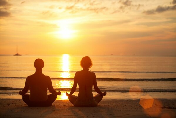 Un hombre y una mujer meditan al atardecer junto al mar