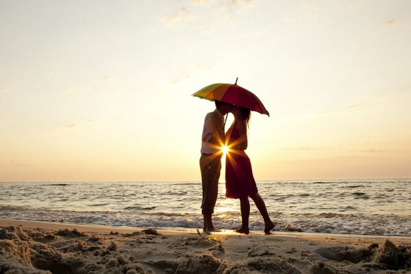 Lovers on the background of sunset on the sea with an umbrella in their hands