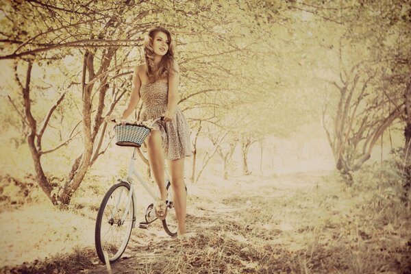 Ragazza in un vestito leggero su una bicicletta con un cestino