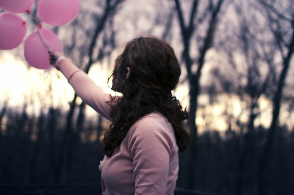 Девушка держит воздушные шары розового цвета взади неё находятся размытый фон