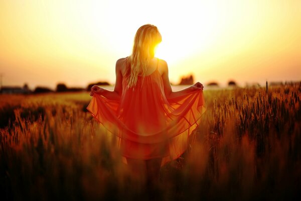 A girl in a red dress at sunset in a field