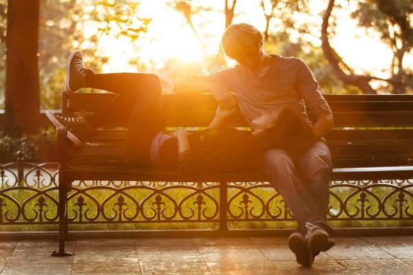 A man and a woman lying on a bench, a couple in love, a warm conversation in nature during the day against the background of trees and the sun