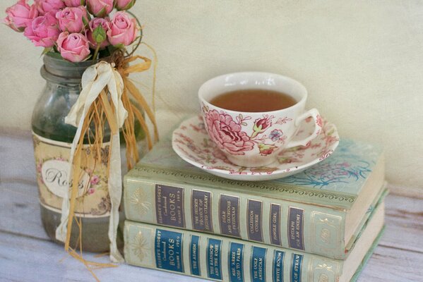 Bouquet de roses roses dans un bocal et couché à côté d un livre avec une tasse de thé