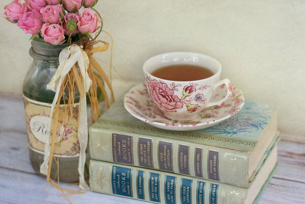 Bukiet różowych róż w słoiku i leżące obok książki z filiżanką herbaty