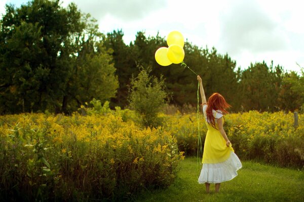 Рыжая девочка в бело-желтом платье с желтыми шариками на поле с высокими желтыми цветами