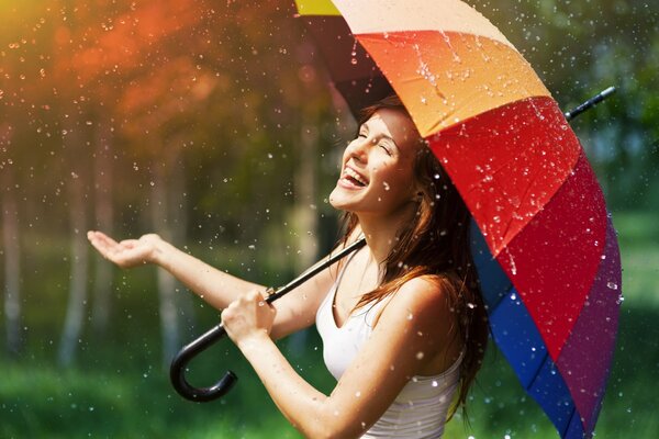 Fille avec un parapluie multicolore se réjouit de la pluie