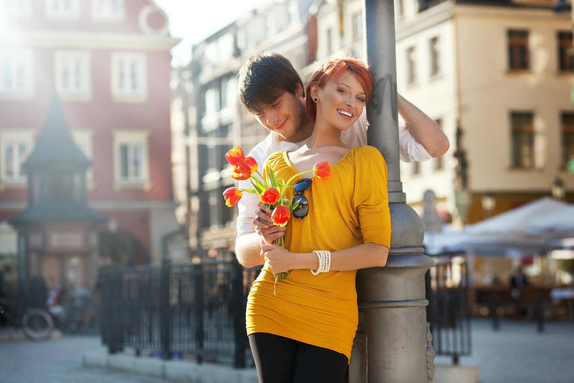 coppia ragazza rossa ragazzo risate sorriso fiori tulipani città recinzione tocco occhiali da sole bicicletta