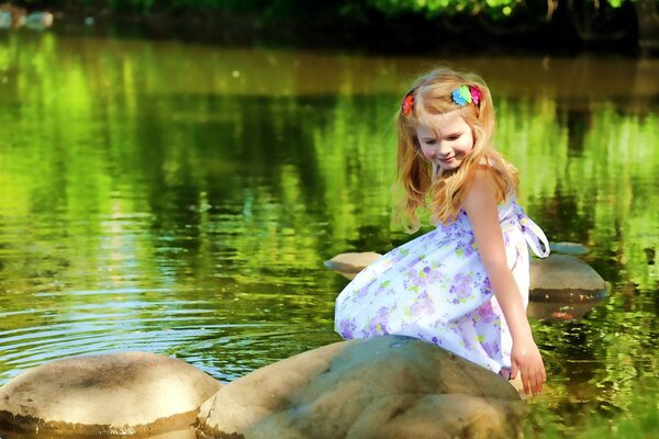 Nella calda estate, è bello sedersi su un ciottolo vicino al lago, anche se sei una bambina