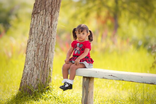 Bambina sulla panchina nella foresta soleggiata