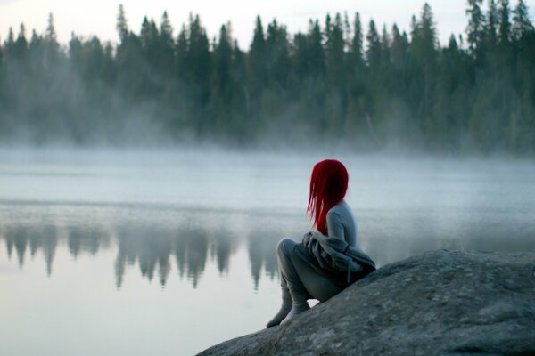 Ein rothaariges Mädchen sitzt am Ufer und schaut in den Nebel