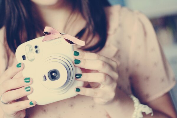 A camera in the hands of a girl with green nails