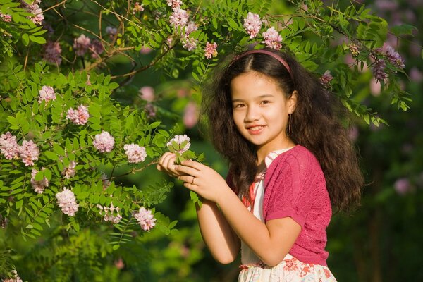 A girl holds a branch of a bush with pink flowers