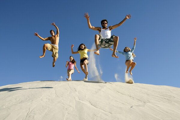 A cheerful company of young people jumps from a sandy hill