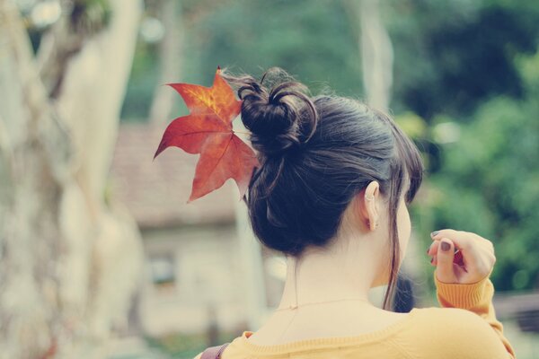 A girl in a yellow sweater with a leaf in her hair