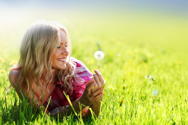 Beautiful girl blodinka smiles holding a dandelion in her hands