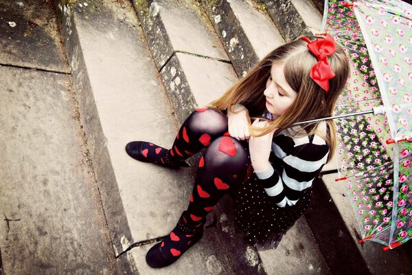 A girl with an umbrella is sitting on the stairs