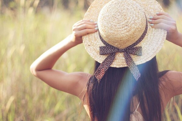 A brown-haired girl poses in a hat on a field in greenery