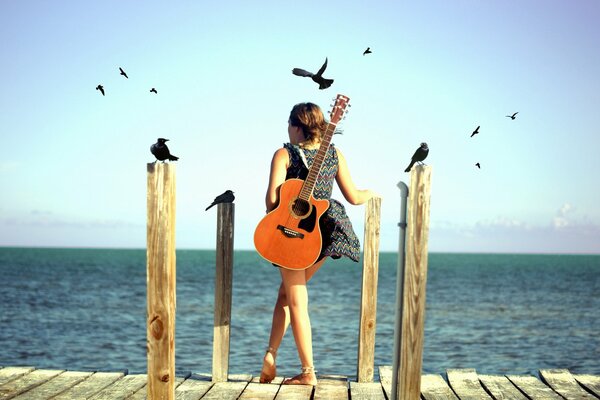 A girl with a guitar stands on the seashore