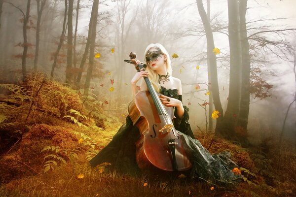 A girl in a mask with a double bass on the background of an autumn forest