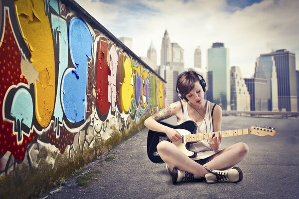 Mädchen mit Kopfhörern an der Wand mit Graffiti spielt Gitarre