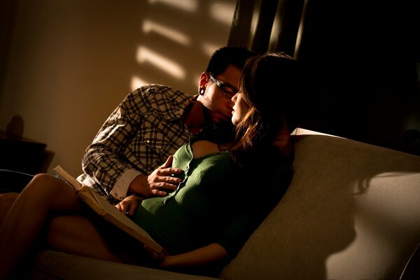 El chico se sienta en el Sofá y abraza a la chica con un escote profundo. Noche romántica en pareja, pasión en los ojos