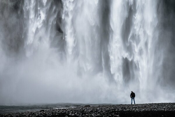 A lone man stands at the waterfall with his head lowered.