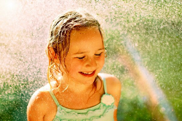 A joyful girl in water drops and a rainbow