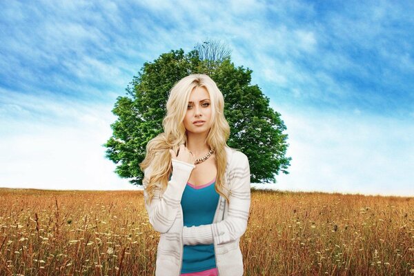 Blonde standing in a meadow against a background of a lonely tree and a blue sky