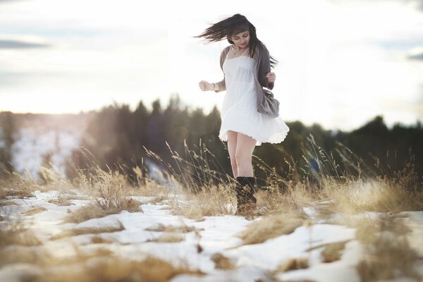 A girl in a dress and boots in a field with melting snow spring