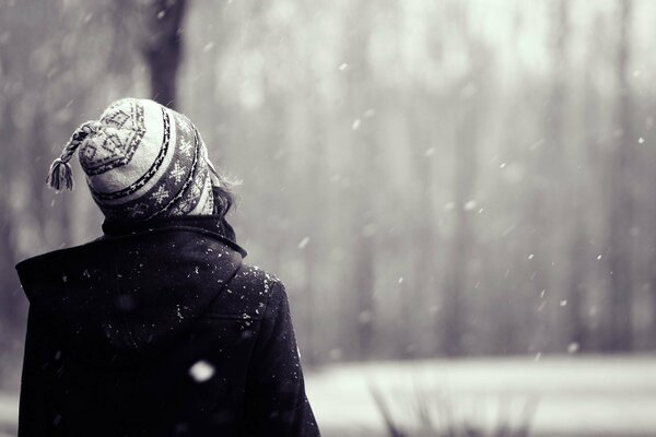 Das Mädchen in der Mütze schaut auf den fallenden Schnee