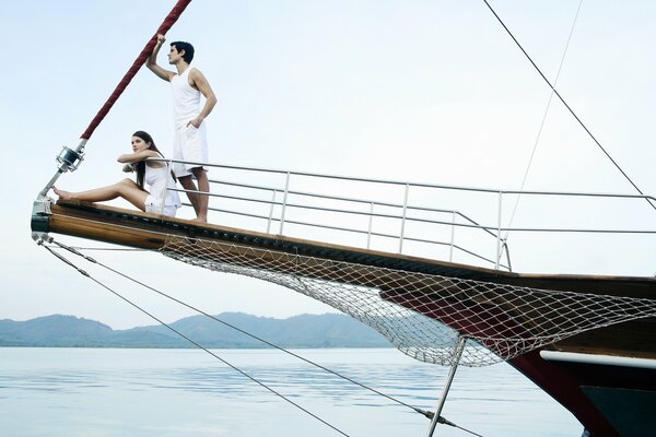 A couple in white on the bow of a luxury yacht peering into the distance