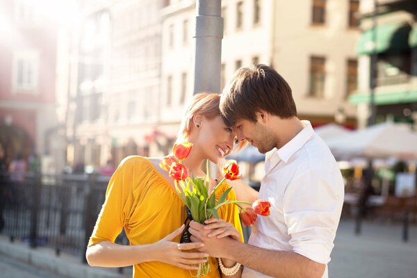 A girl and a guy on a romantic date on a sunny day in the city with a bouquet of red tulips