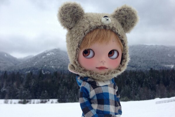 A doll in a winter warm hat on a background of snow