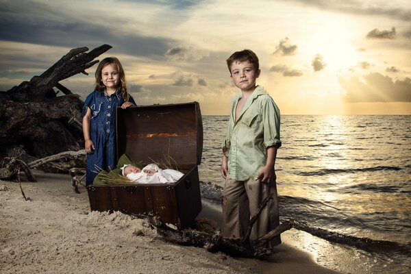 Brother and sister are photographed with a newborn baby on the seashore