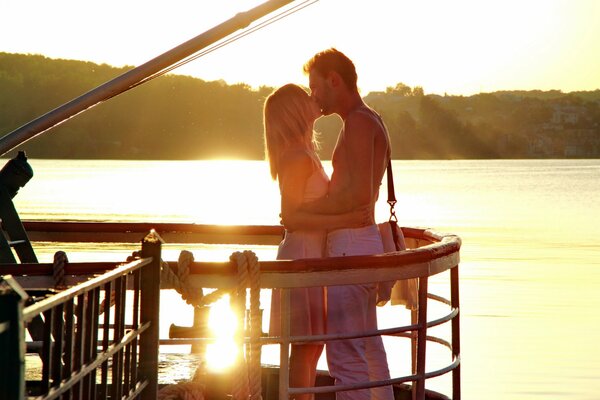 Sur la rive de la rivière, un couple amoureux dans les rayons du coucher du soleil