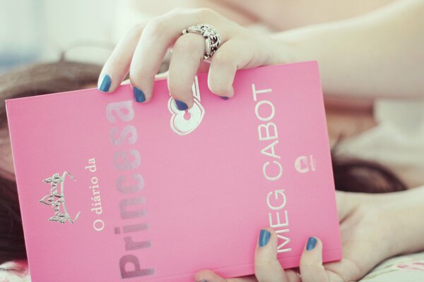 The girl is holding a pink book in her hands