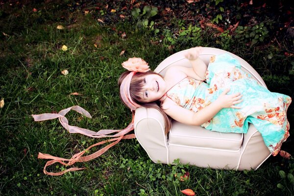 A girl with ribbons on her head is lying in a chair in nature