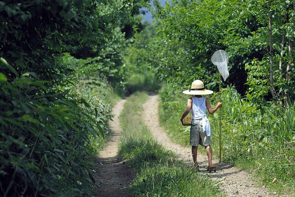 Un niño con un sombrero y una red caminando por un camino