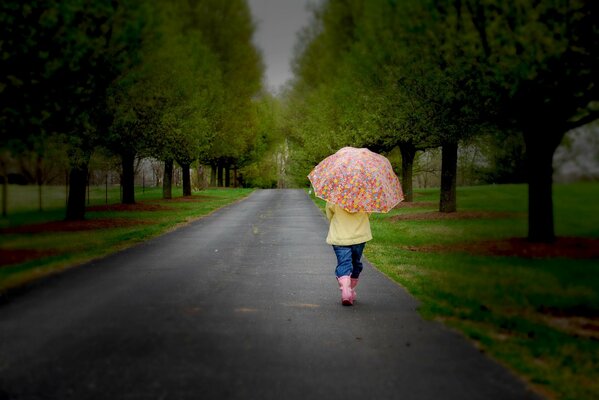 Petite fille marche sur la route avec un parapluie